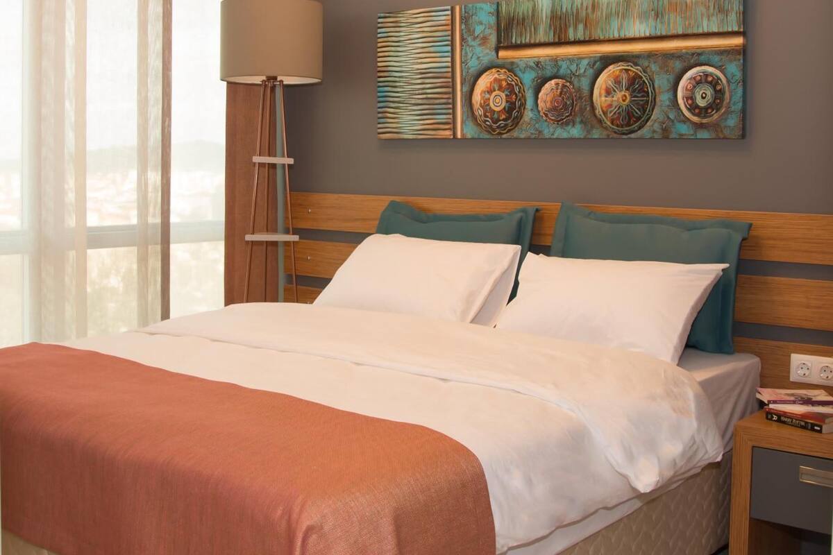 A hotel room with a bed, a nightstand, an air conditioner, and a window with curtains.