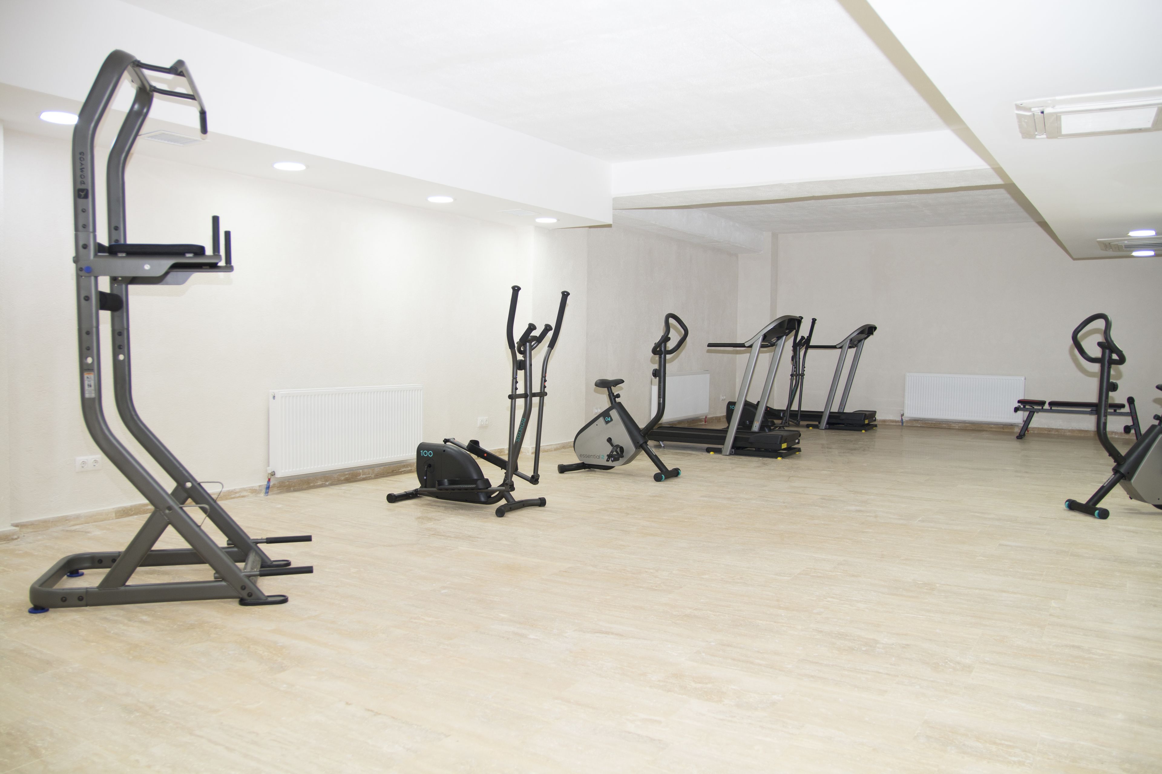 A spacious room with a wooden floor and white walls, equipped with various exercise machines including a stair climber, elliptical, and stationary bikes.