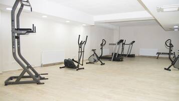 A spacious room with a wooden floor and white walls, equipped with various exercise machines including a stair climber, elliptical, and stationary bikes.