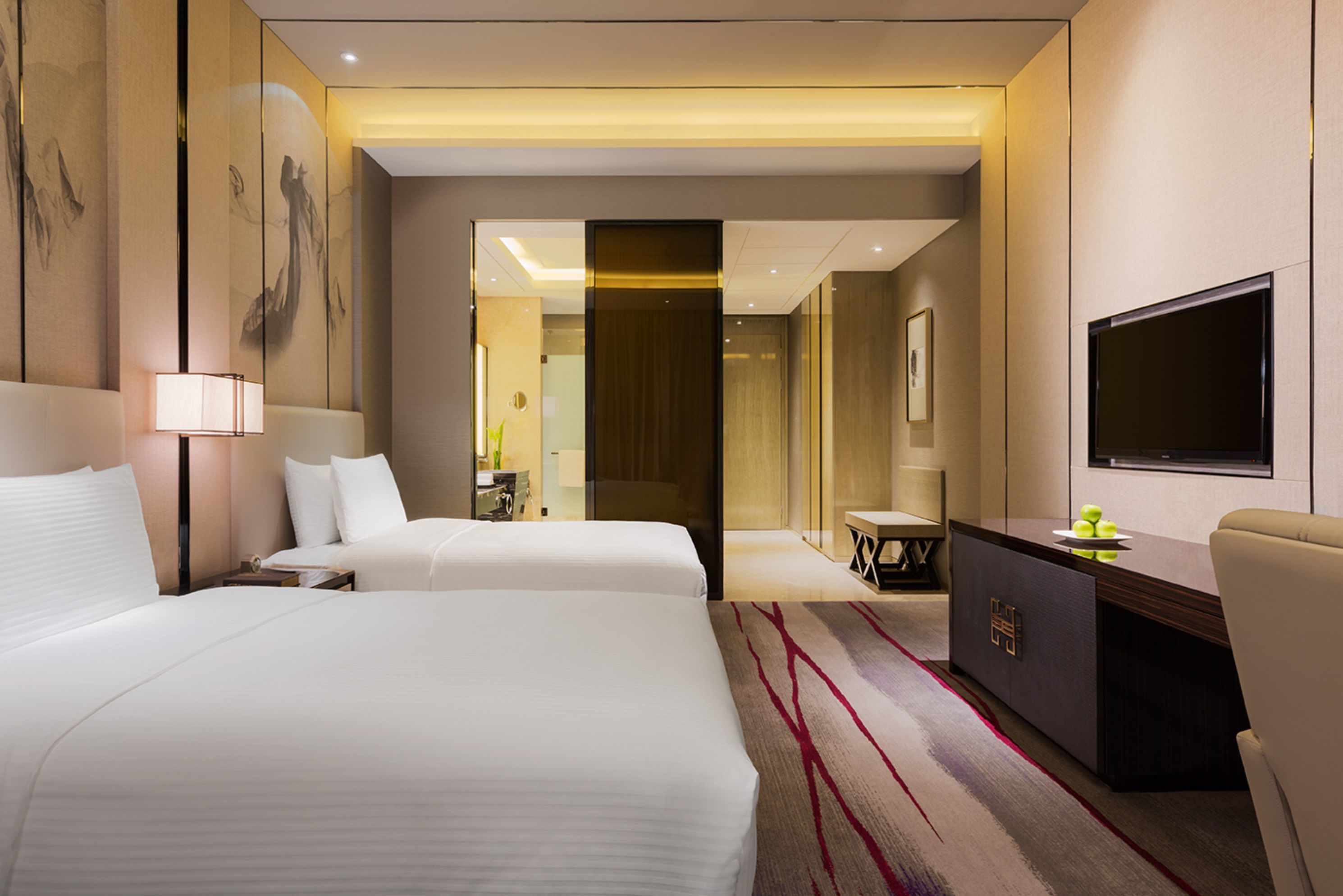 A hotel room with two beds, a desk, a TV, and a large mirror.