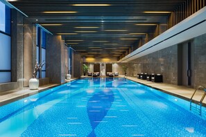 Une piscine intérieure moderne au design épuré, avec un grand bassin rectangulaire à l’eau d’un bleu cristallin, dont la surface reflète les lumières du plafond.