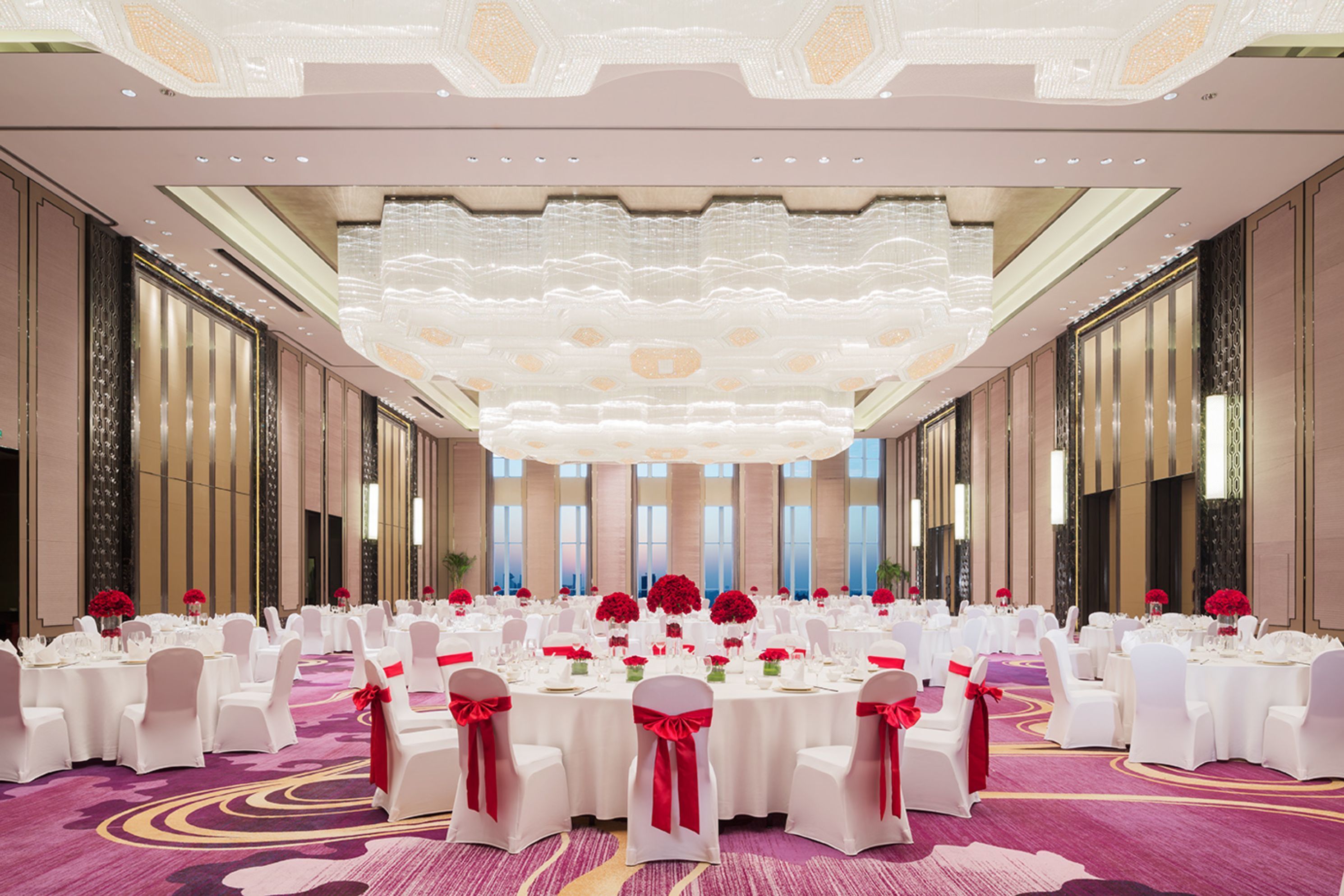A large banquet hall with round tables, white chairs, and red sashes.