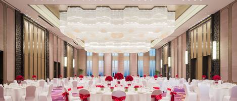 A large banquet hall with round tables, white chairs, and red sashes.