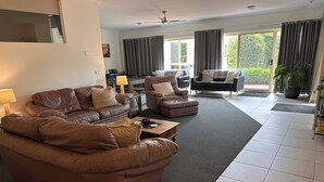 A spacious living room with leather sofas, a coffee table, and a dining area with a table and chairs. - Austral Place 88 via Merri River (Dennington)