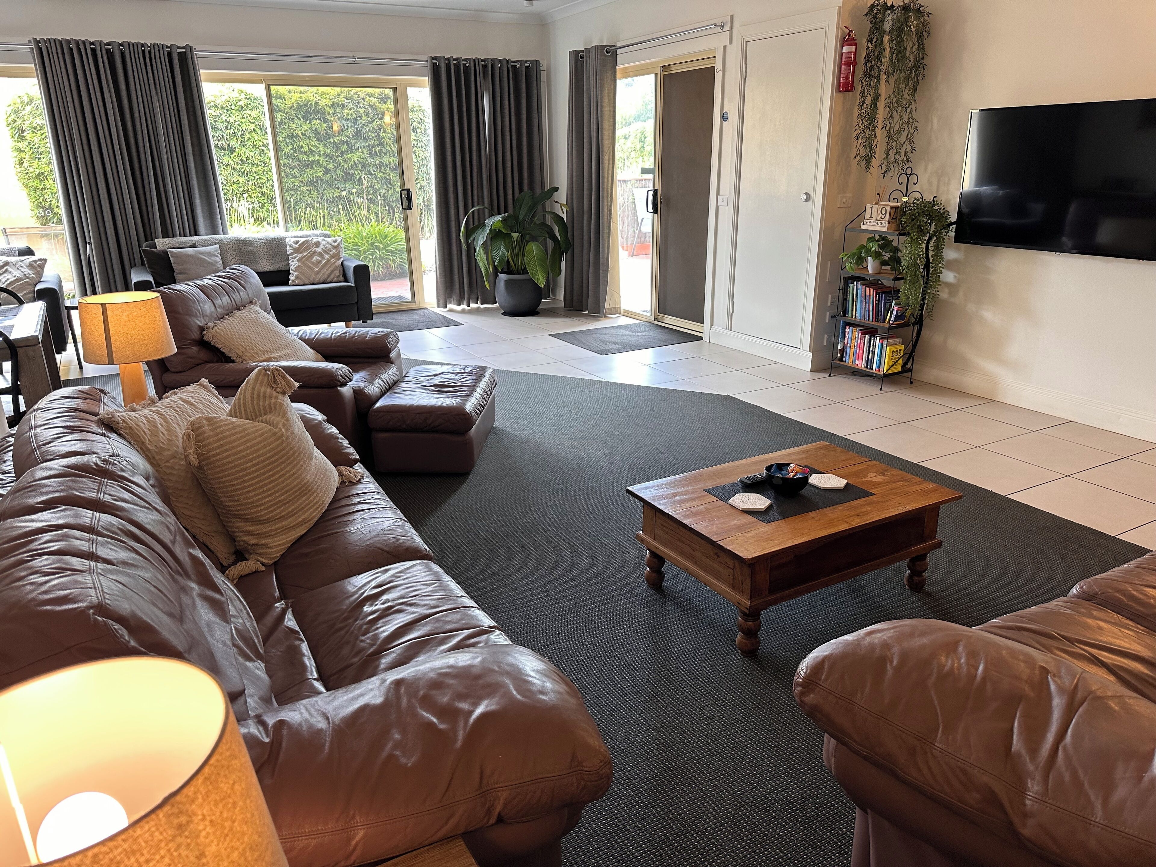 A spacious living room with a leather sofa, a wooden coffee table, and a television on the wall.