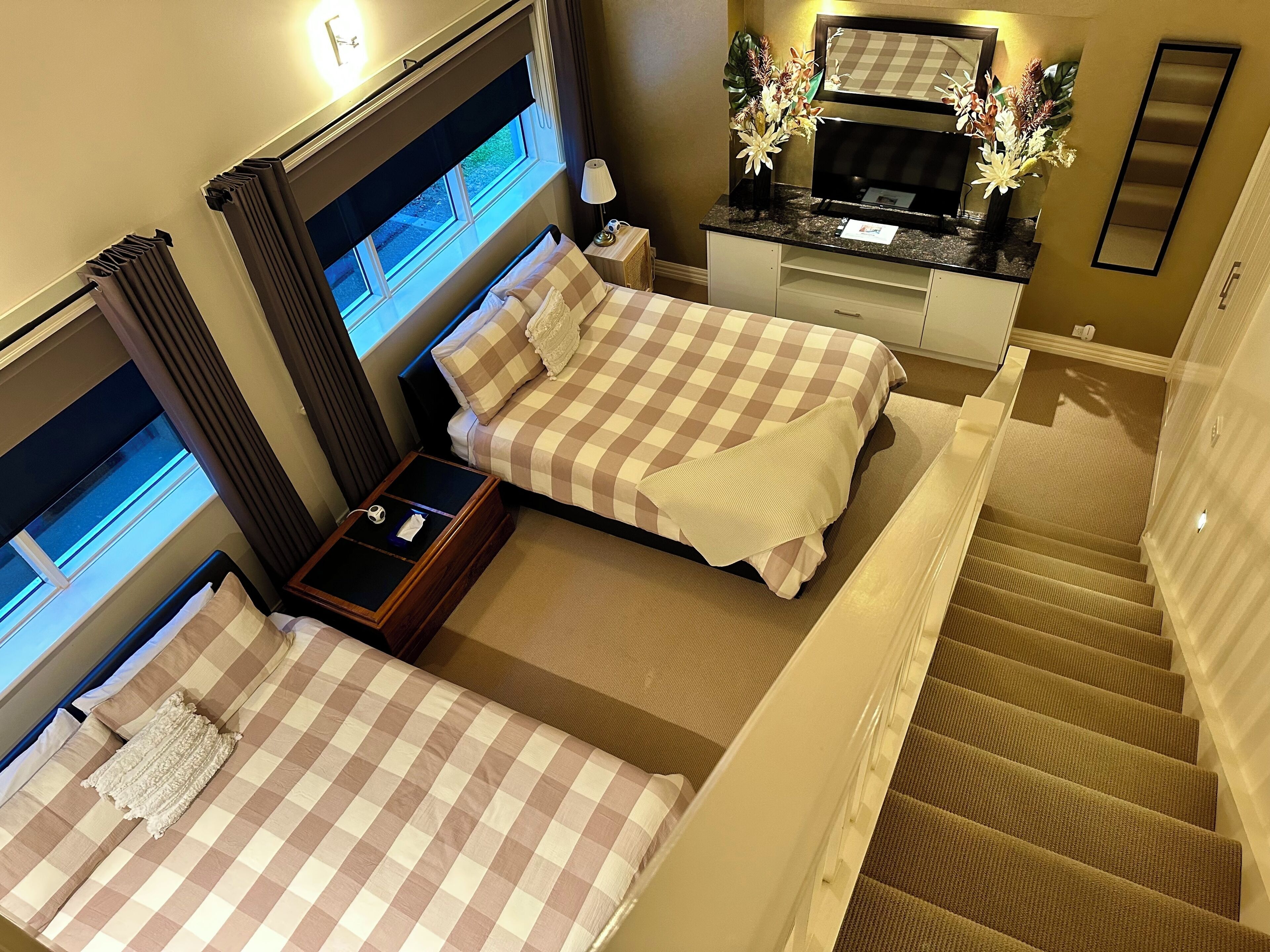 Habitación de hotel con dos camas, una mesita, una mesita de noche, un espejo y una escalera.