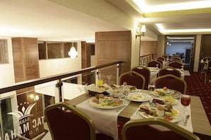Une salle à manger d’hôtel avec plusieurs tables préparées pour le petit-déjeuner, proposant une variété de plats et de boissons.