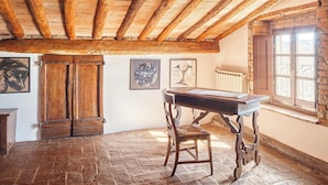 A rustic room with exposed wooden beams, a stone floor, a wooden table with a chair, and a window with a view.
