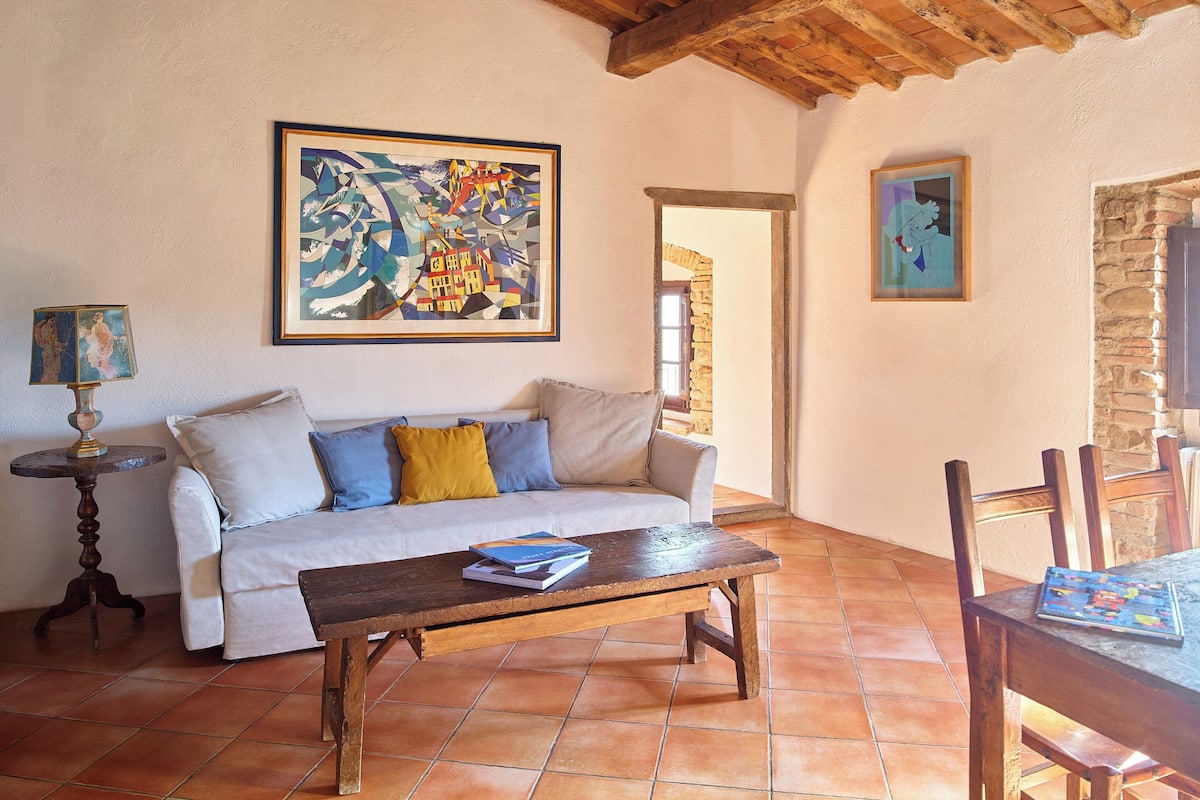 Una sala de estar con un sofá, una mesa de centro, una lámpara y dos obras de arte enmarcadas en la pared.