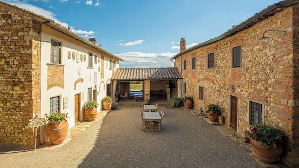 A courtyard with stone buildings, a central table, and potted plants.