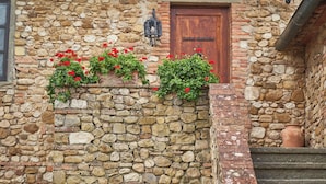 A stone building with a wooden door labeled "Bulli Cottage." There are flower boxes with red flowers on the stone wall.