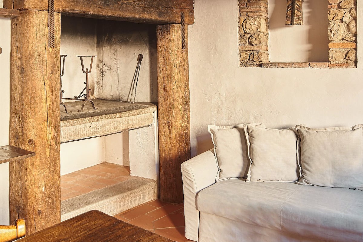Un interior rústico con una mesa de madera, un sofá blanco, una pared de piedra y una estructura de techo de madera.