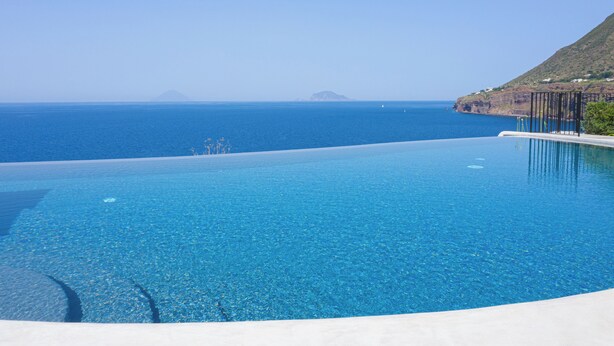 Piscina infinita de color azul intenso con vista al océano y a islas distantes.