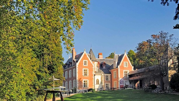 A large, historic building with multiple gabled roofs and a well-maintained lawn in front.