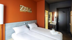 A hotel room with a large bed, a bedside table, a mirror, and a wall with a 'Zzz' sign.