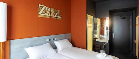 Habitación de hotel con una cama grande, una mesita de noche, un espejo y una pared con un cartel que dice 'Zzz'.