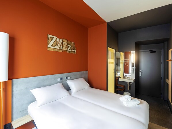 Habitación de hotel con una cama grande, una mesita de noche, un espejo y una pared con un cartel que dice 'Zzz'.