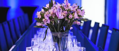 A conference table with a vase of flowers, surrounded by chairs and empty wine glasses.