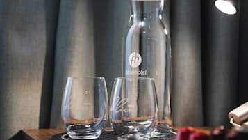 A clear glass decanter and two glasses on a wooden surface with a dark curtain in the background.