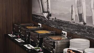Un mostrador de buffet con diferentes opciones de comida, una estación de café y un cuadro grande de un velero en la pared.