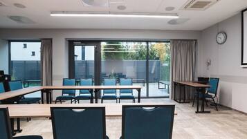 Un salón de conferencias con una mesa grande, sillas, un reloj y vistas a través de puertas de cristal.