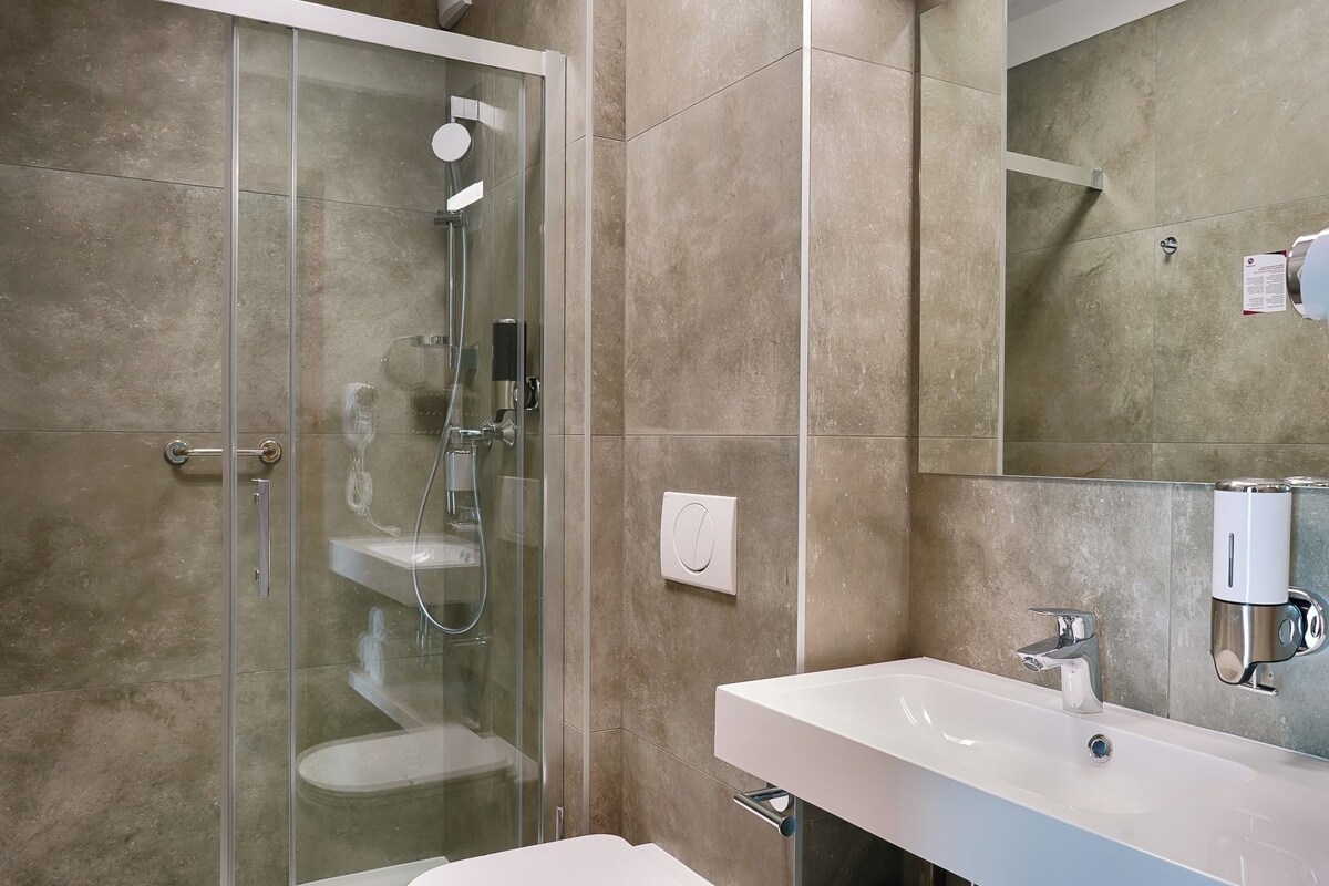 A modern bathroom with a glass-enclosed shower, a white sink, and a large mirror.