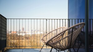 A balcony with a view of a cityscape, featuring a wicker chair and a metal railing. - Hotel Focus Poznań (Poznan)