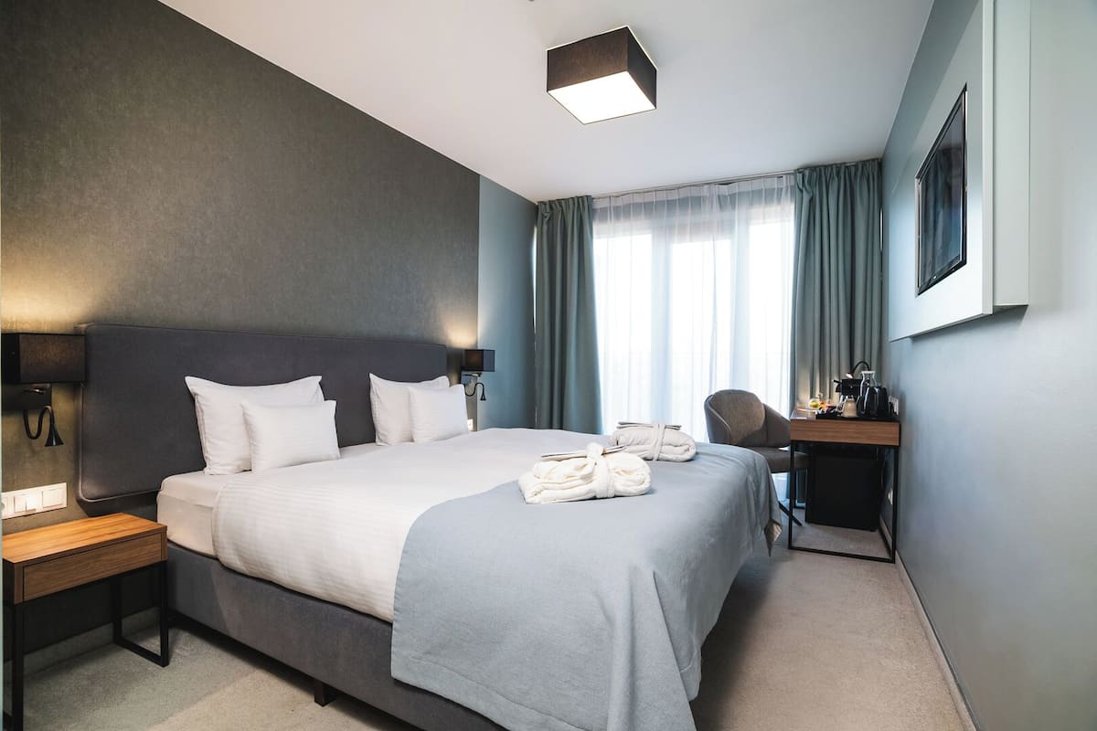 Una habitación de hotel con una cama grande, un escritorio, una silla, una lámpara y una ventana con cortinas.