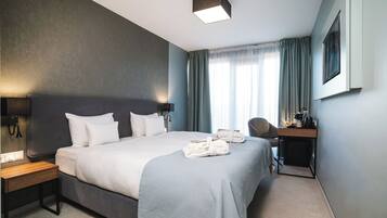 Una habitació d'hotel amb un llit gran, una taula de treball, una cadira, una làmpada i una finestra amb cortines.