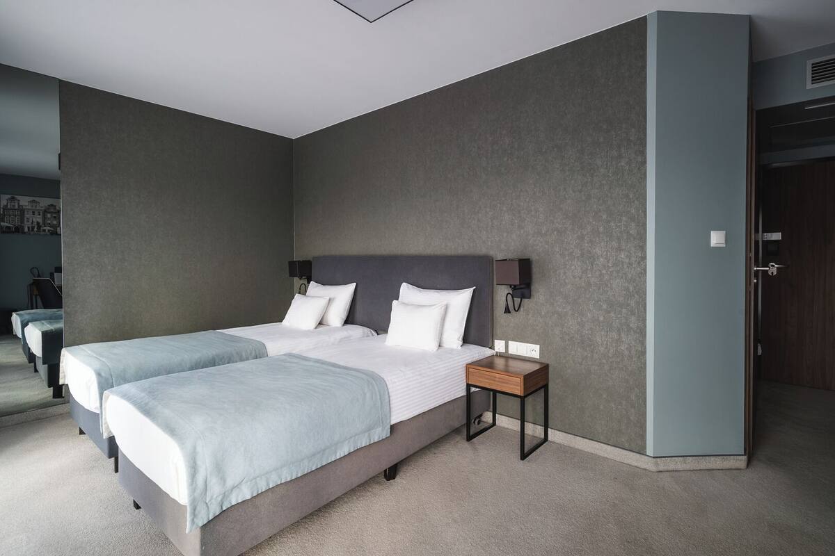 Una habitación de hotel moderna con dos camas, una mesita de noche y una lámpara de pared.