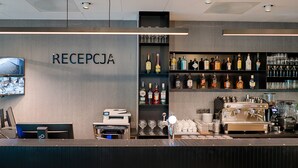 A reception area with a counter, a coffee machine, and shelves with various bottles and glasses. - Hotel Focus Poznań (Poznan)