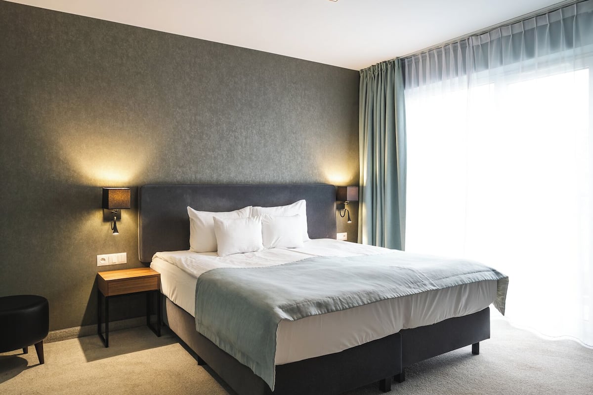 Habitación de hotel con cama, mesitas de noche, lámparas fijadas a la pared y vistas al exterior.