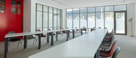 A conference room with a long table and chairs, large windows, and a red accent wall.