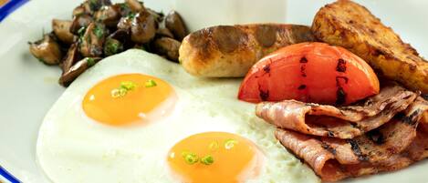 A plate with eggs, bacon, sausages, mushrooms, roasted tomatoes, and baked beans.
