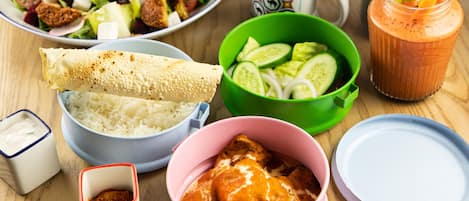 Ein Tisch mit verschiedenen Speisen, darunter ein Salat, eine Reisportion, eine Curry-Schale, ein Gebäckröllchen und ein Smoothie.