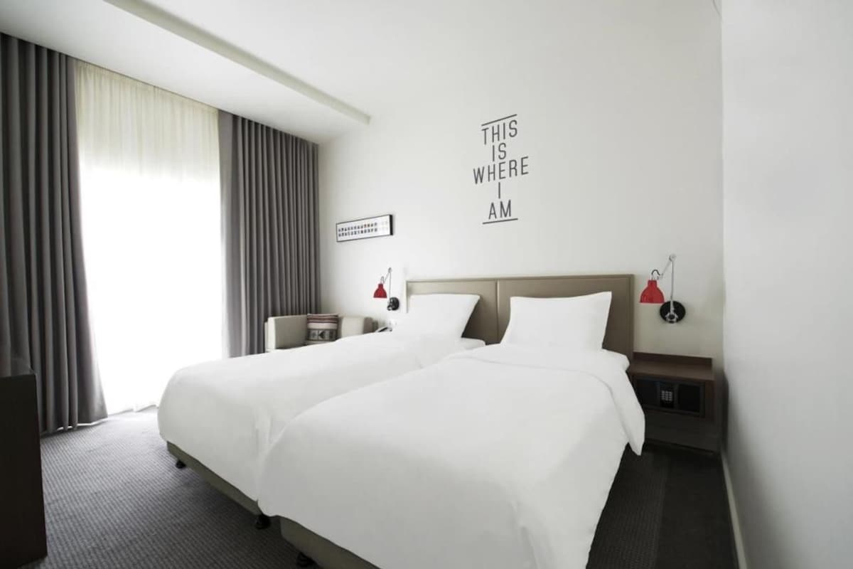 A hotel room with two beds, a nightstand, a lamp, and a wall sign.