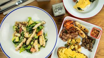 A table with three plates of food, including a salad, eggs benedict, and a mix of meats and vegetables.