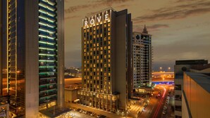 Ein Hochhaus-Hotel mit beleuchtetem Schriftzug "ROVE" an der Fassade, umgeben von anderen Gebäuden und einer belebten Straße im Abenddämmerung.