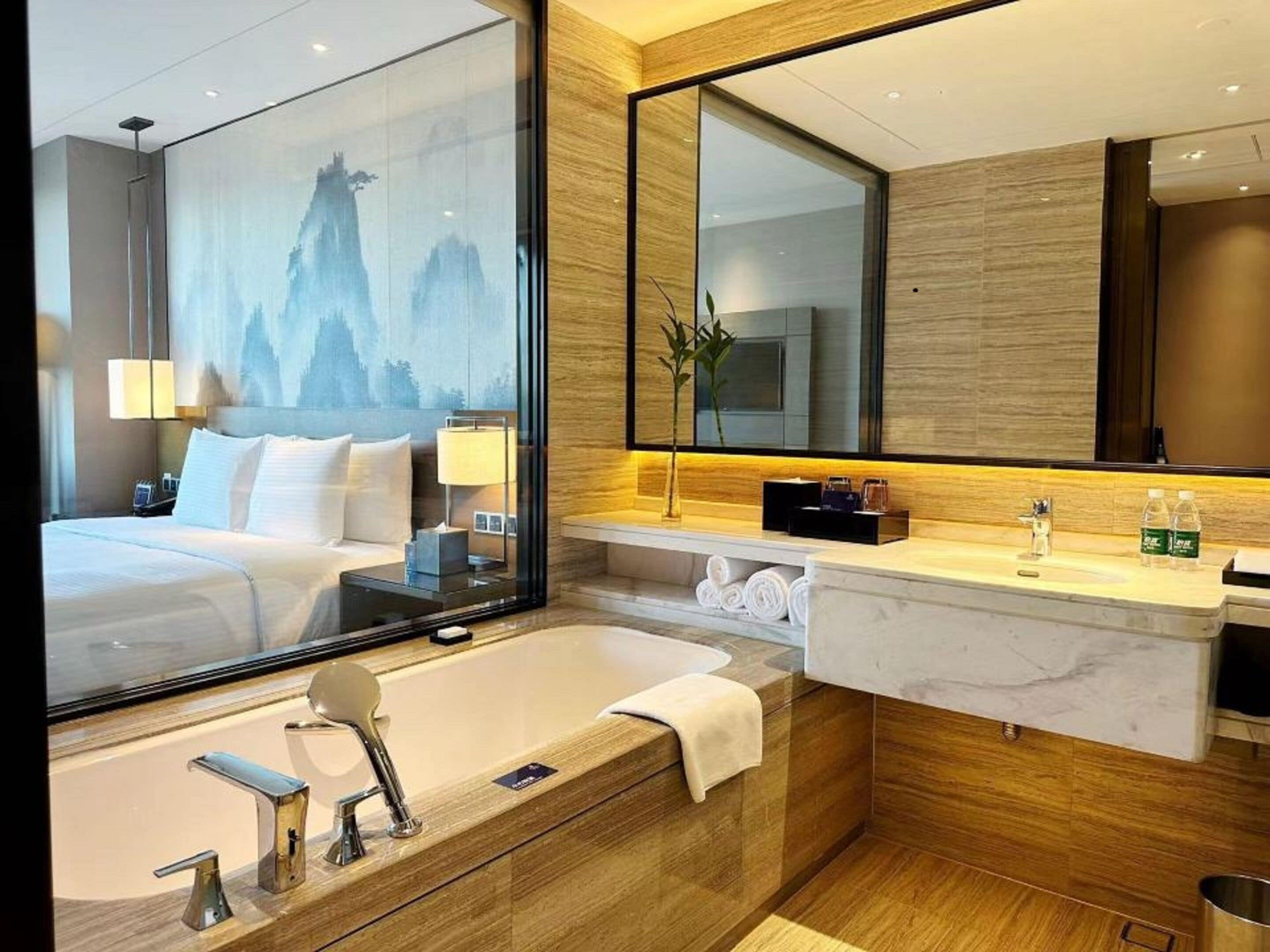 Una habitación de hotel moderna con una cama grande, un ba ño con bañera, un tocador con espejo y un ventanal con vistas a la montaña.