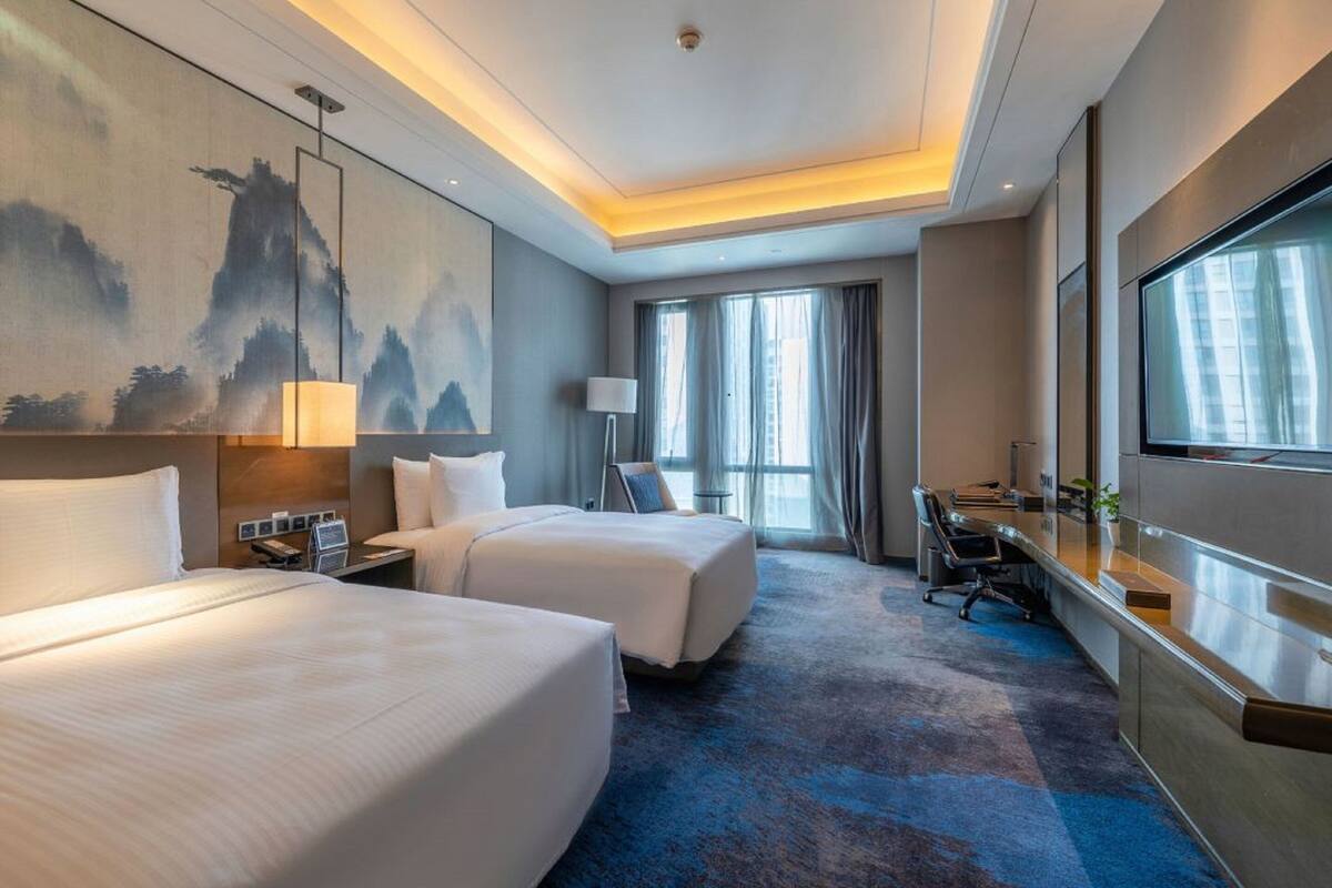 Ein Hotelzimmer mit zwei Betten, einem Schreibtisch, einem Fernseher und einem Bild an der Wand.