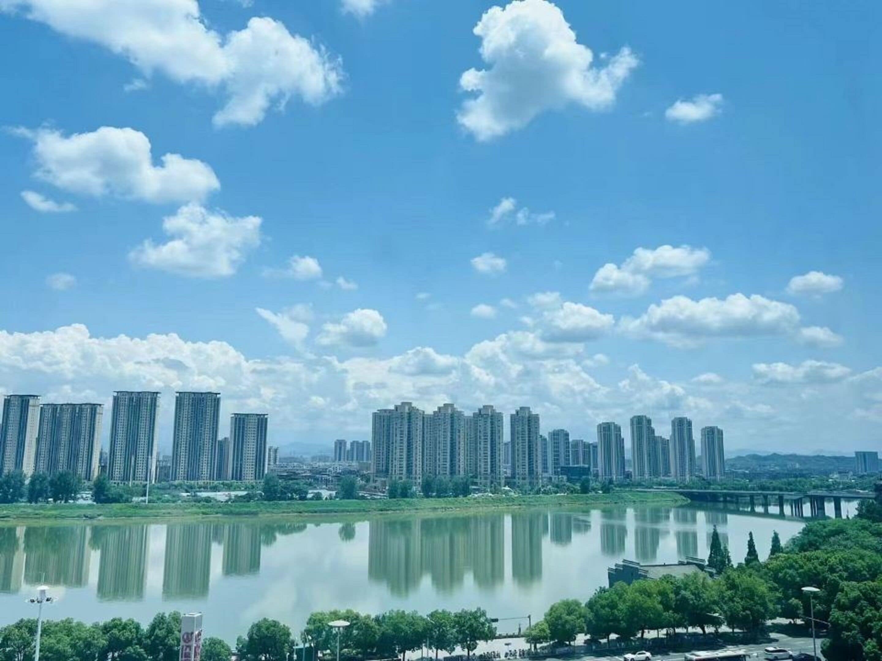 Un paisaje urbano con rascacielos, un lago tranquilo y un cielo azul despejado.