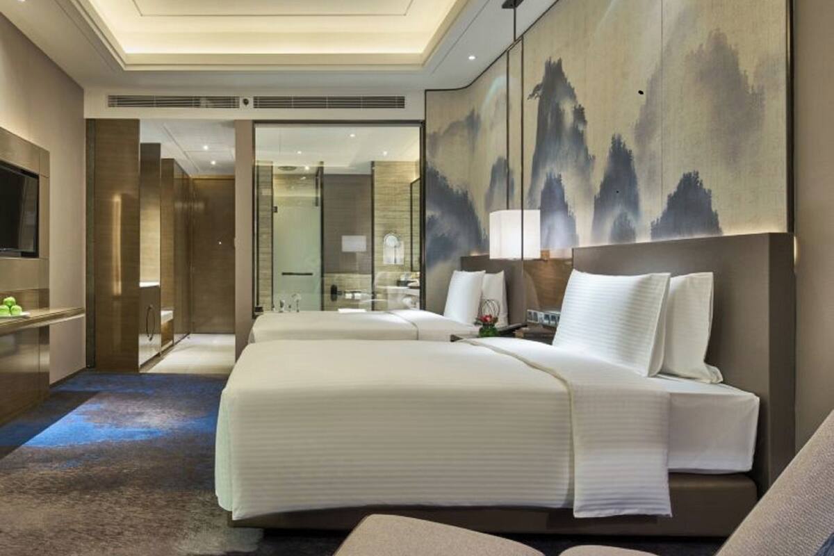 Ein modernes Hotelzimmer mit einem großen Bett, einer Sitzecke, einem Fernseher und einem Badezimmer mit Glasdusche.