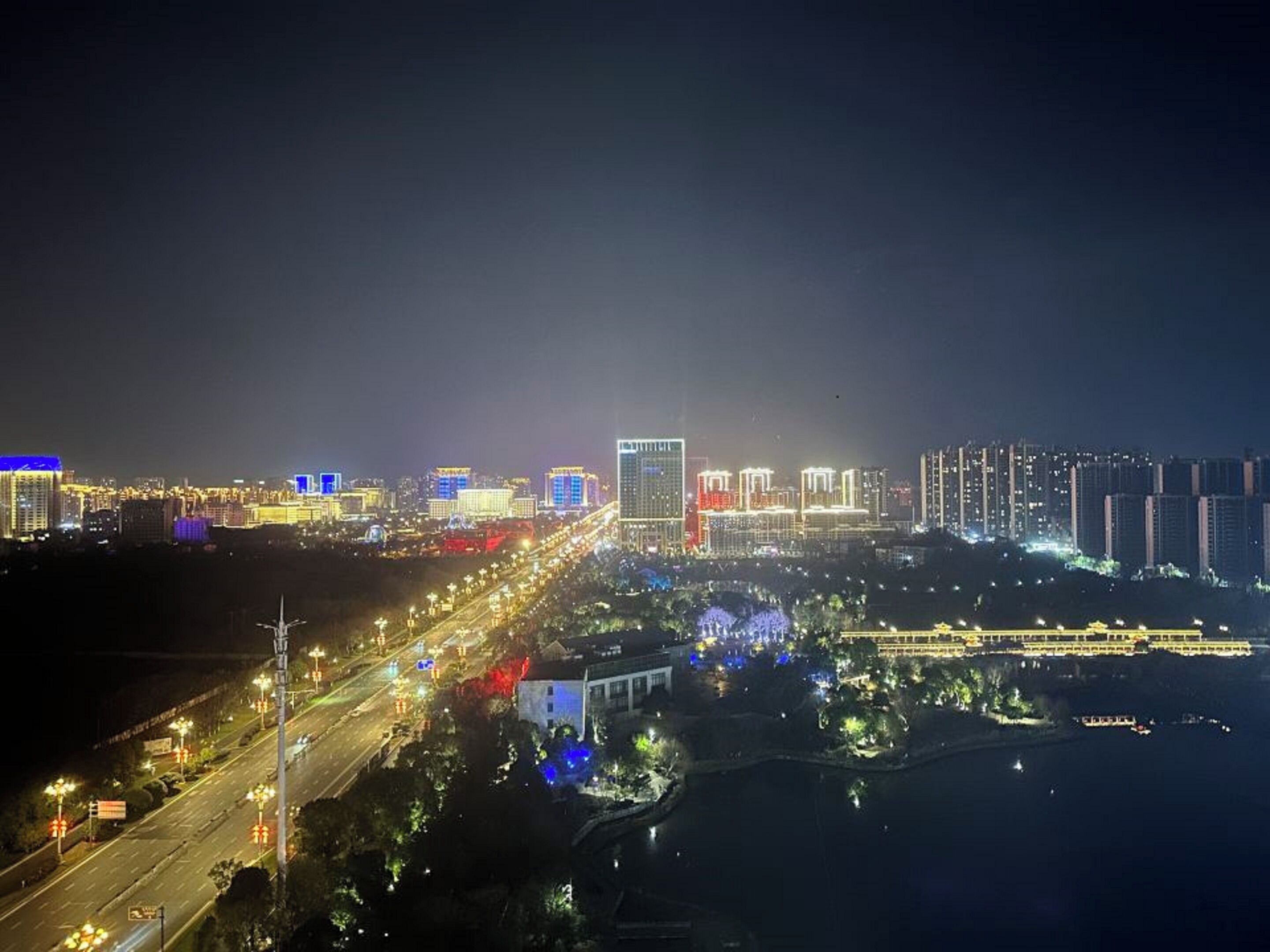 Un paisaje urbano nocturno con edificios iluminados, un puente y un río.