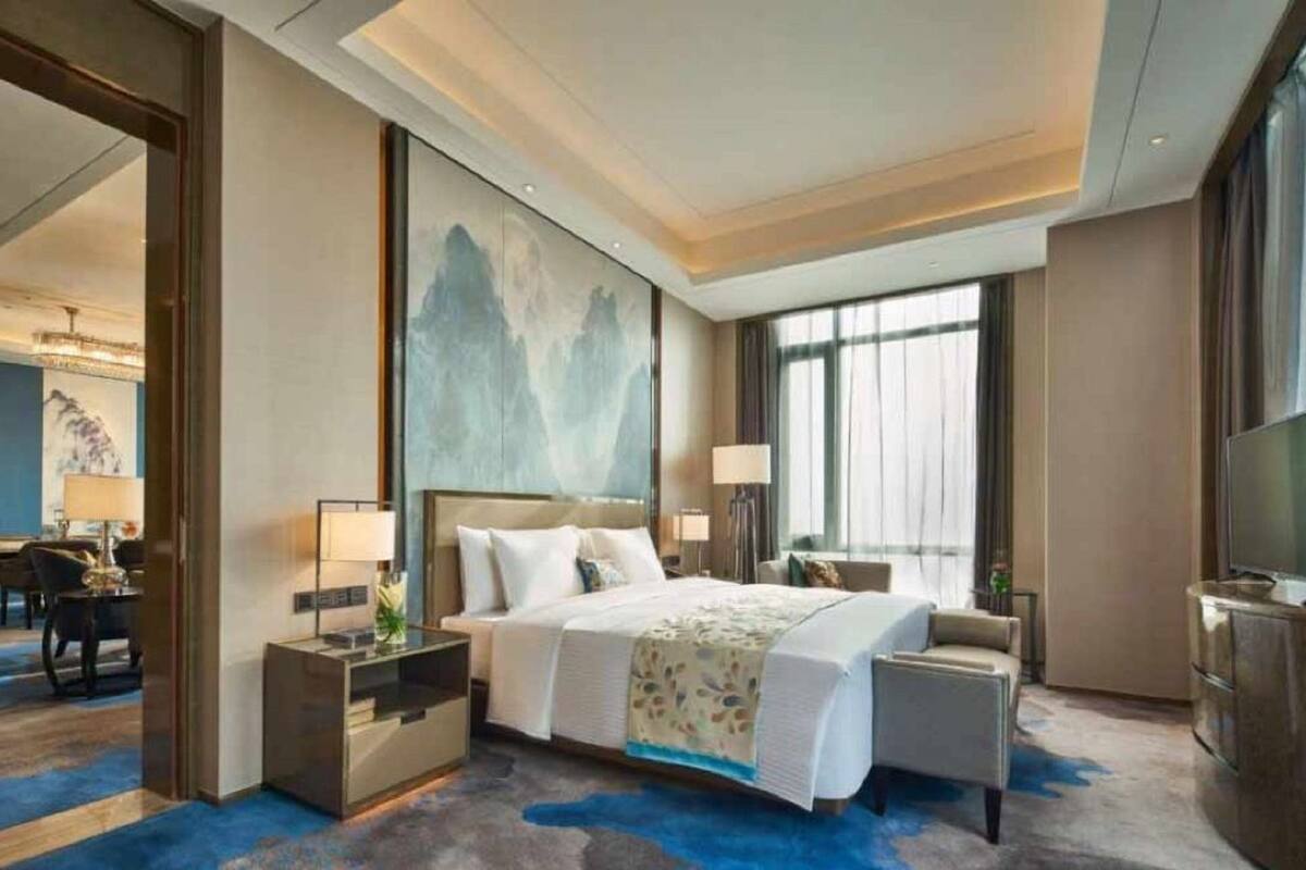 Ein Hotelzimmer mit einem großen Bett, einem Schreibtisch, einem Sessel, einem Fernseher und einem Bild an der Wand.