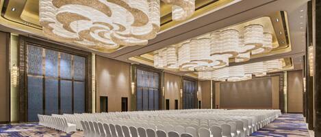 A large conference room with rows of white chairs, a patterned carpet, and ornate ceiling lights.