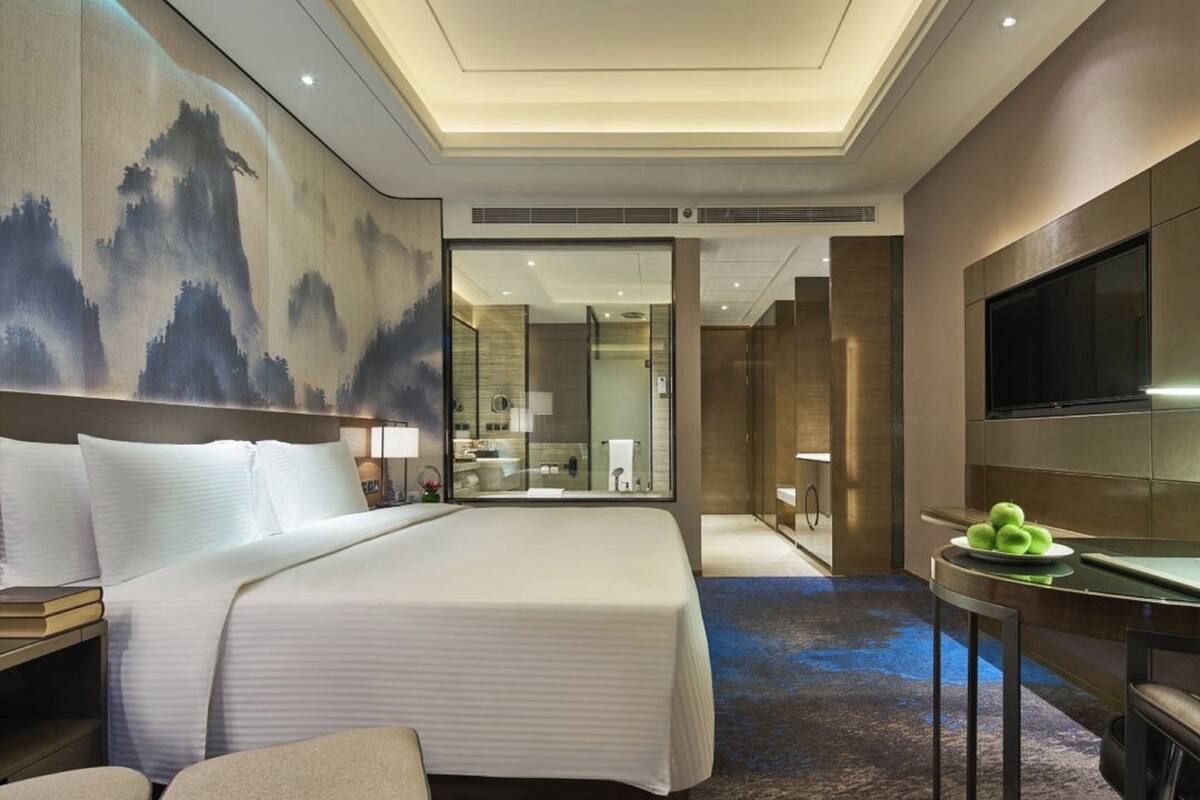 Ein modernes Hotelzimmer mit einem großen Bett, einem Flachbildfernseher, einem Schreibtisch mit Stuhl und einem Bild an der Wand.