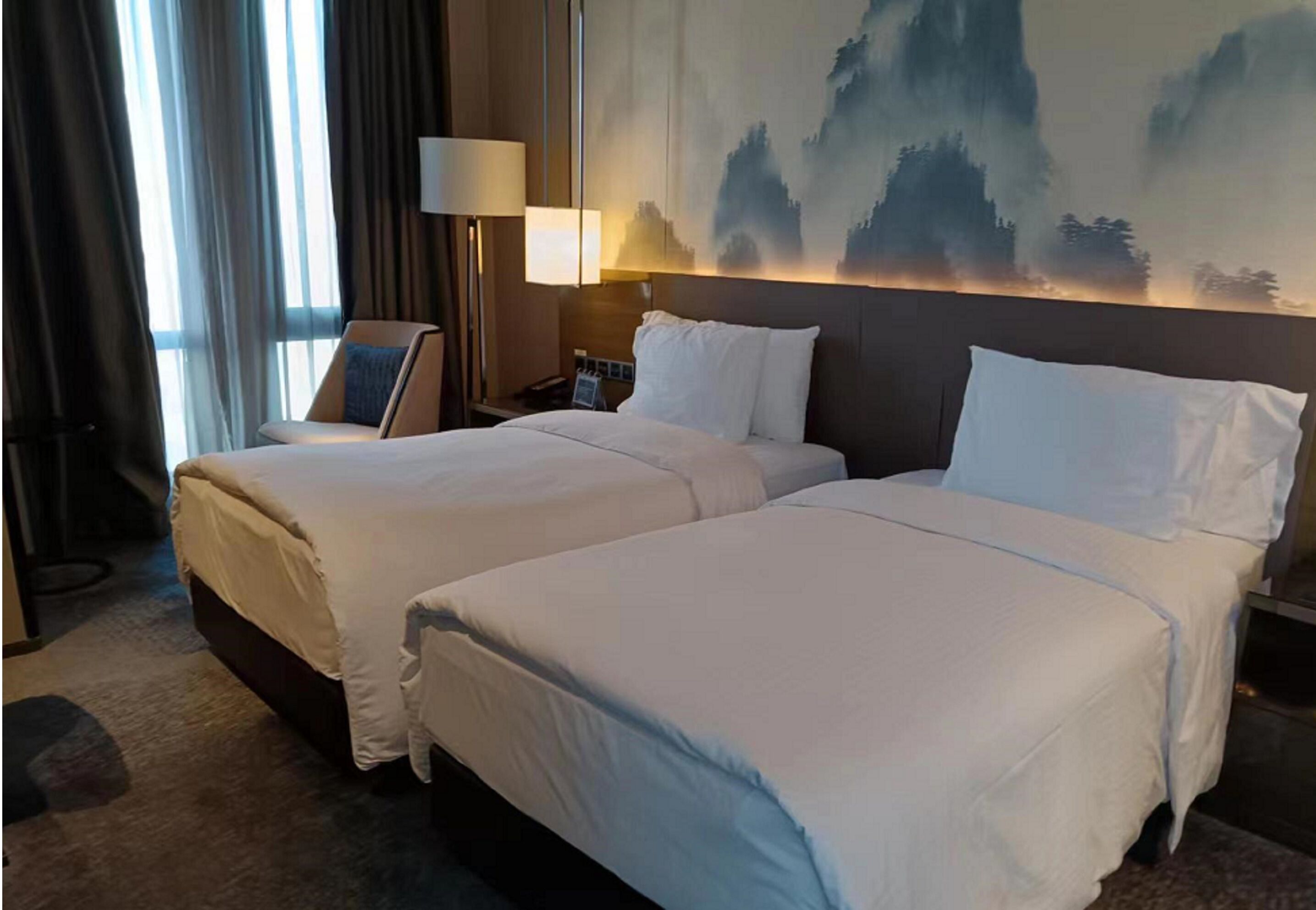 A hotel room with two beds, a large painting on the wall, and a nightstand with a lamp.