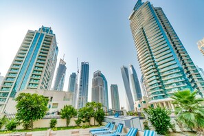 A high-rise building with a modern design, surrounded by lush greenery and a pool area with lounge chairs. - 2 Bedroom Apartment Marina (Dubai)
