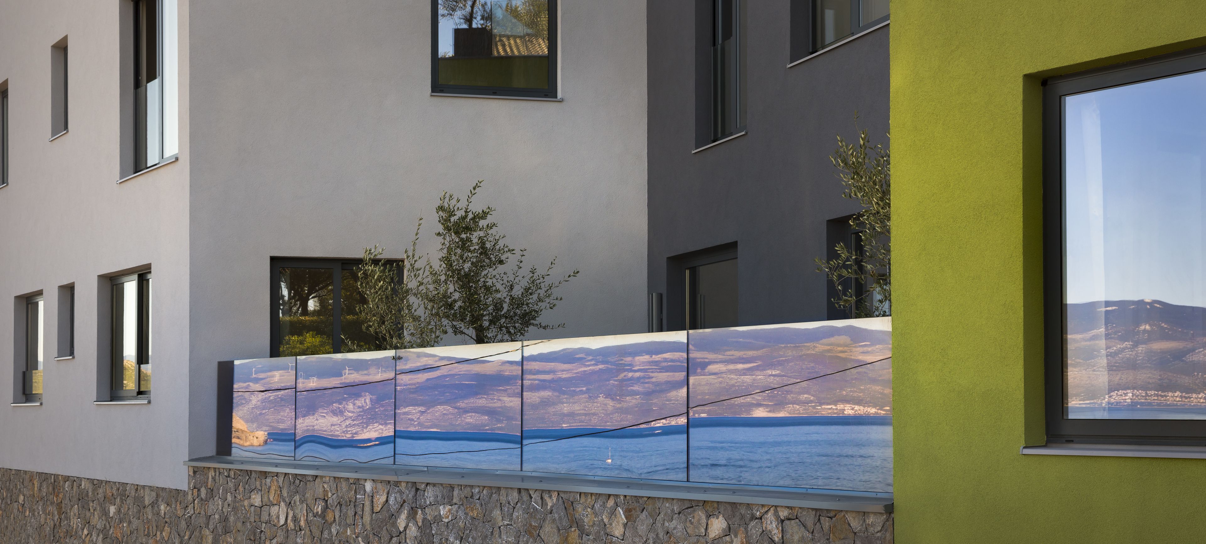A modern building with a stone base, large windows, and a mural of a coastal landscape.