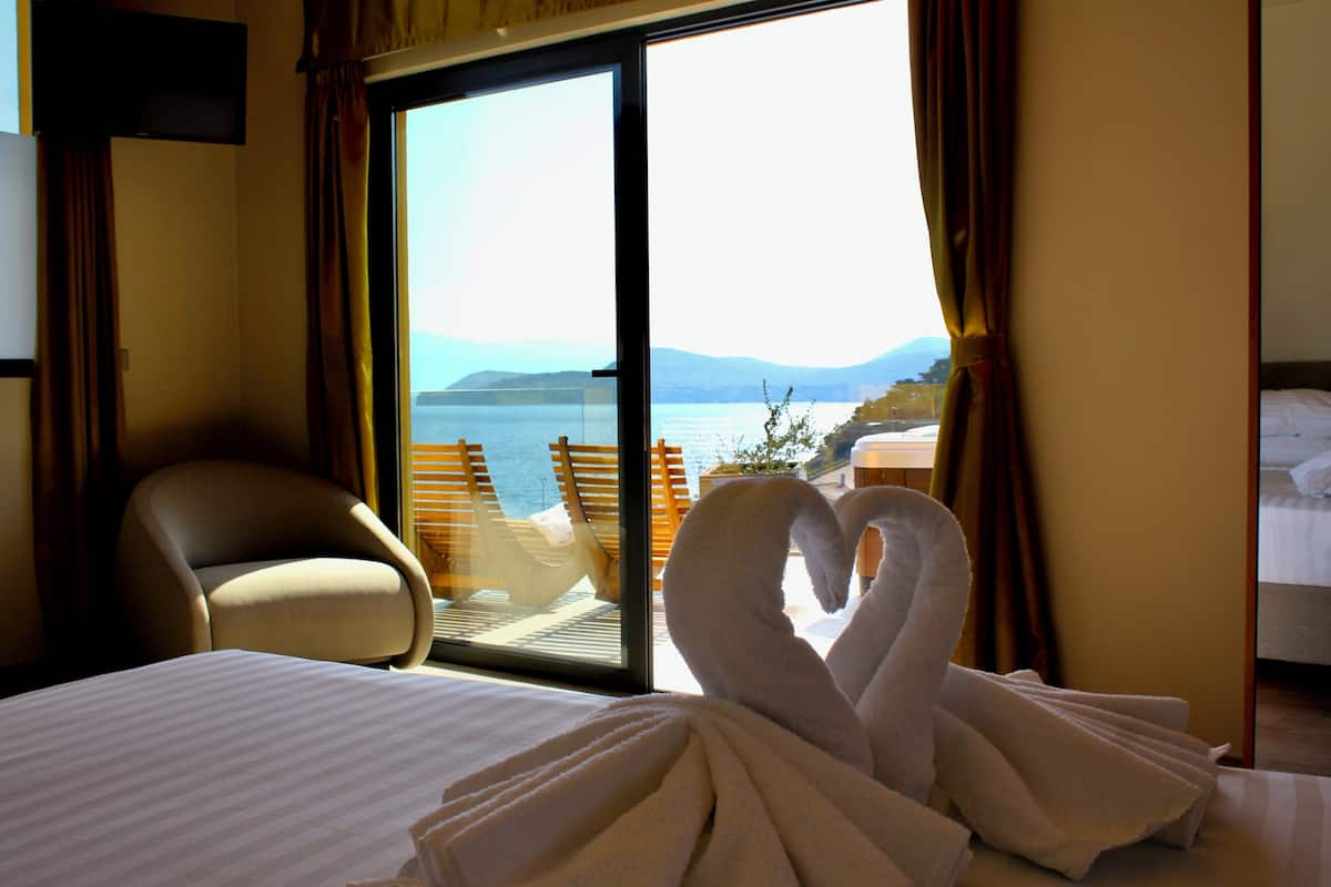 Una habitación de hotel con cama, una silla, un ventanal con vista al mar y dos toallas con forma de cisne sobre la cama.